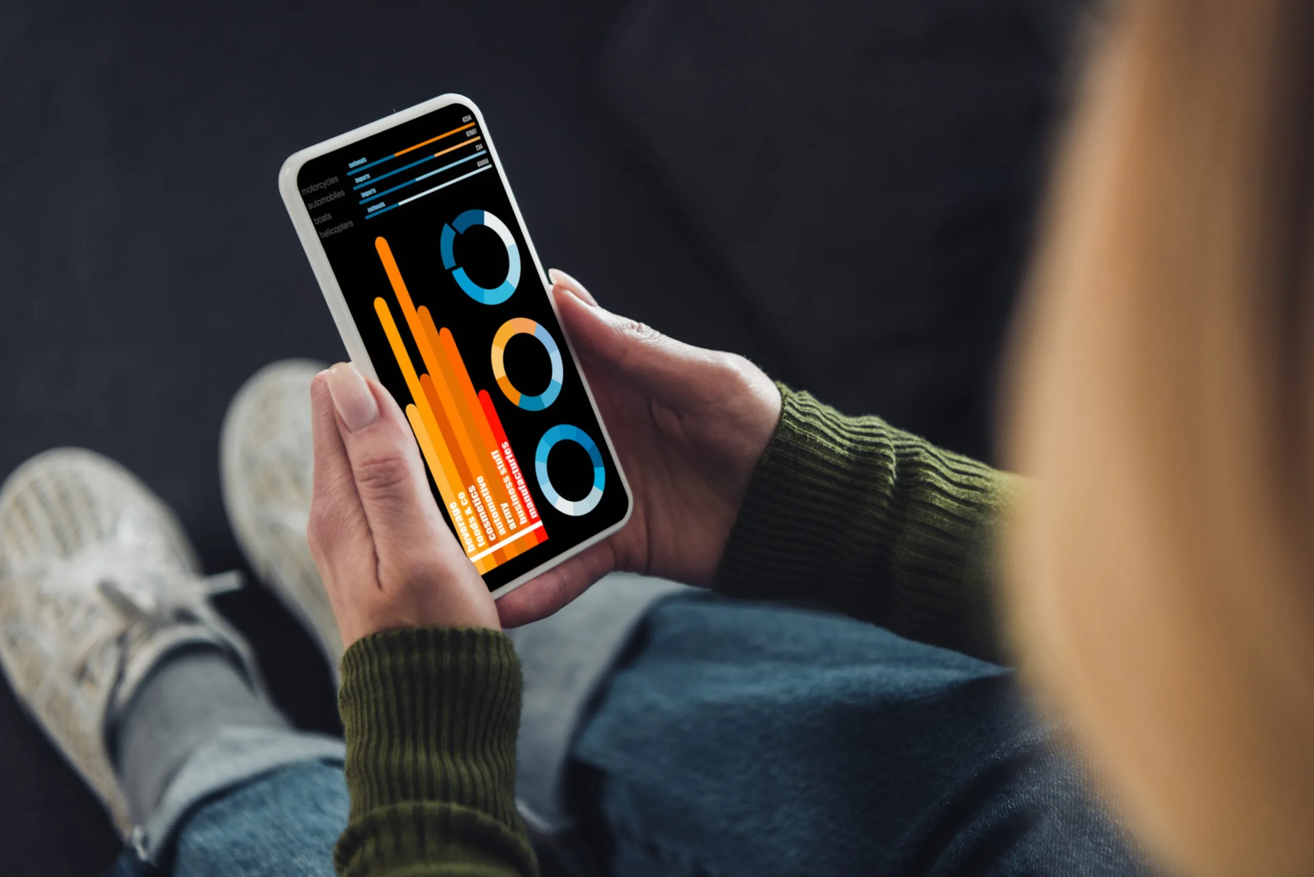 Persona sosteniendo un smartphone con gráficos y estadísticas financieras en pantalla, imágen del artículo sobre aplicaciones en tendencia